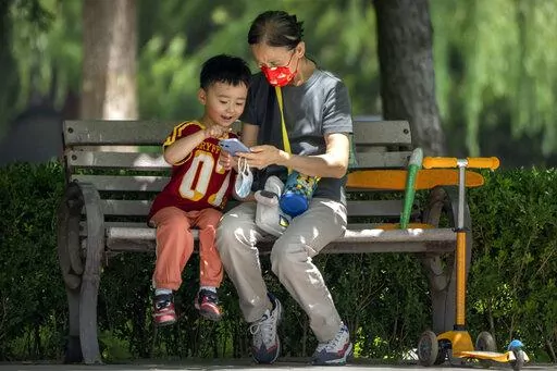 A woman wearing a face mask and a child look at a cellphone as they sit on a bench at a public park in Beijing, on June 2, 2022. As the week-long Lunar New Year holidays in China draw near with promises of feasts and red envelopes stuffed with cash, children have yet another thing to look forward to - one extra hour of online games each day. (AP Photo/Mark Schiefelbein, File)