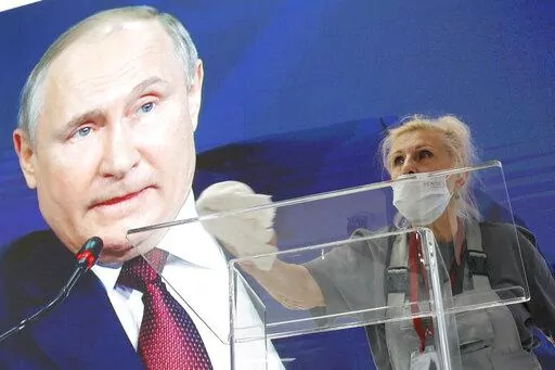 A worker cleans a speaker's podium as Russian President Vladimir Putin seen on a screen in the background at the St. Petersburg International Economic Forum in St. Petersburg, Russia, June 4, 2021. Russia’s showpiece investment gathering begins Thursday, June 16, 2022 and organizers are telling foreign participants to be sure to bring cash — not necessarily for making investments, but for spending money. The advice for the St. Petersburg International Economic Forum is a quiet acknowledgment