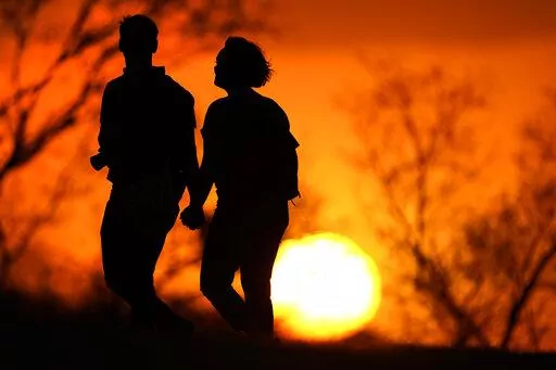 In this March 10, 2021 file photo, a couple walks through a park at sunset in Kansas City, Mo. U.S. life expectancy dropped for two consecutive years in 2020 and 2021, marking the first such trend since the early 1920s, according to a new government report. (AP Photo/Charlie Riedel, File)