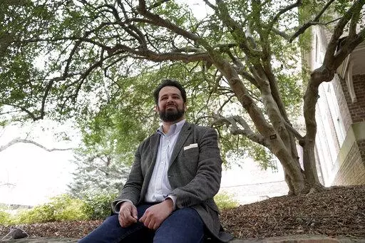 Benjamin Frey, American Studies professor at the University of North Carolina, sits under the native Ilex vomitoria tree on campus in Chapel Hill, N.C., Thursday, Feb. 24, 2022. Frey, a member of the Eastern Band of Cherokee Indians, led the language research behind a new smartphone interface by Lenovo-owned Motorola. The Cherokee language interface on its newest line of phones, uses the syllable-based written characters first created by the Cherokee Nation's Sequoyah in the early 1800s. (AP Pho