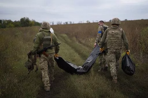 Ukrainian servicemen carry a bag containing the body of a Ukrainian soldier, center, as one of them, right, carries the remains of a body of a Russian soldier in a retaken area near the border with Russia in Kharkiv region, Ukraine, Saturday, Sept. 17, 2022. (AP Photo/Leo Correa)