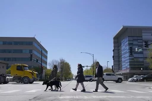 Maureen Reid, left, and her guide dog, Gaston, cross the intersection of Wood Street and Roosevelt Avenue with Sandy Murillo, center, and Geovanni Bahena, relying on an audible signal for the blind, on April 26, 2023, in Chicago. The U.S. Census Bureau wants to change how it asks people about disabilities, and some advocates are complaining that they were not consulted enough on what amounts to a major overhaul in how disabilities would be defined by the federal government. (AP Photo/Charles Rex