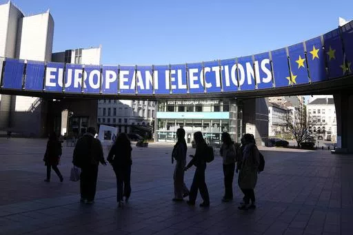 A group stands under an election banner outside the European Parliament in Brussels on April 29, 2024. In an increasingly vitriolic political climate, the last thing needed in the runup to the June European Union elections was an assassination attempt on one of the bloc’s most controversial figures. (AP Photo/Virginia Mayo, File)