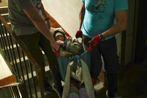 Roman Zhylenkov, left, and another volunteer of Vostok SOS charitable organisation carry an elderly woman from her home during an evacuation in Kramatorsk, eastern Ukraine, Thursday, May 26, 2022. Volunteer drivers are risking everything to deliver humanitarian aid to Ukrainians behind the front lines of the war — and to help many of them escape. The routes are dangerous and long and the drivers risk detention, injury or death. (AP Photo/Francisco Seco)
