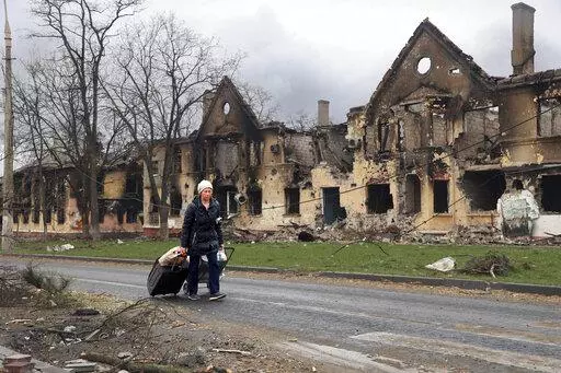 A woman pulls her bags past houses damaged during fighting in eastern Mariupol, Ukraine, Friday, April 8, 2022. Ukraine says it is investigating a claim that a poisonous substance was dropped on the besieged city of Mariupol. Deputy Defense Minister Hanna Maliar said Tuesday, April 12, 2022 it was possible that phosphorus munitions — which cause horrendous burns but are not classed as chemical weapons — had been used.  (AP Photo/Alexei Alexandrov, file)