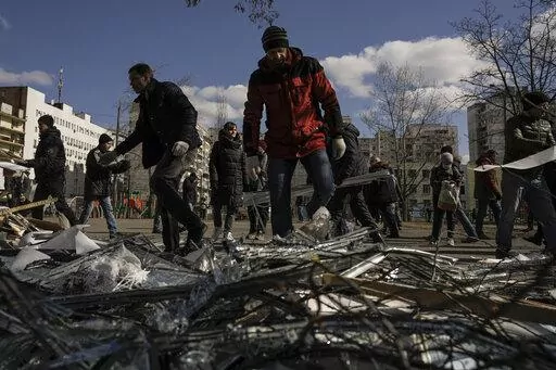 People clear debris outside a medical center damaged after parts of a Russian missile, shot down by Ukrainian air defense, landed on a nearby apartment block, according to authorities, in Kyiv, Ukraine, Thursday, March 17, 2022. Russian forces destroyed a theater in Mariupol where hundreds of people were sheltering Wednesday and rained fire on other cities, Ukrainian authorities said, even as the two sides projected optimism over efforts to negotiate an end to the fighting. (AP Photo/Vadim Ghird