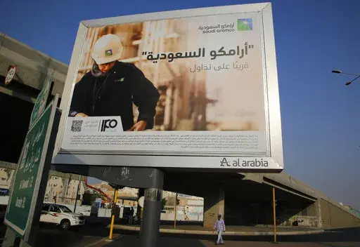 A man walks under a billboard displaying an advertisement for Saudi Arabia's state-owned oil giant Aramco with Arabic reading "Saudi Aramco, soon on stock exchange" in Jiddah, Saudi Arabia on Nov. 12, 2019. Oil giant Saudi Aramco said Sunday, May 15, 2022 its profits soared more than 80% in the first three months of the year, as the state-backed company cashes in on the volatility in global energy markets and soaring oil prices following Russia’s invasion of Ukraine. (AP Photo/Amr Nabil, File)