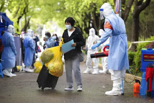 In this photo released by Xinhua News Agency, a villager carrying baggage is disinfected as she returns home after being quarantined due to local COVID cases found in Lianqin Village of Beicai Town in Pudong New Area, Shanghai on Tuesday, April 26, 2022. Shanghai city authorities said Wednesday they will start rounds of COVID-19 testing over the next few days to determine which neighborhoods can safely be allowed a limited amount of freedom of movement, as residents in Beijing watch carefully on
