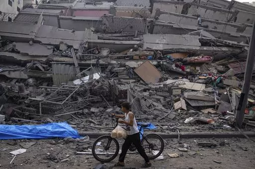 A Palestinian child walks with a bicycle by the rubble of a building after it was hit by an Israeli airstrike, in Gaza City, Sunday, Oct. 8, 2023. A new U.N. report paints a stark picture of the devastating collapsing Palestinian economy after a month of war and Israel’s near total siege of Gaza. (AP Photo/Fatima Shbair, File)