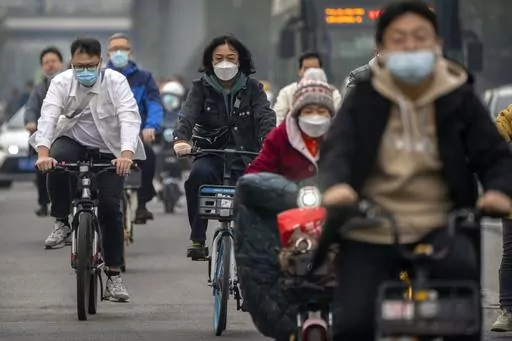 Commuters wearing face masks ride bicycles along a street in the central business district in Beijing, Thursday, Oct. 20, 2022. The World Health Organization downgraded its assessment of the coronavirus pandemic on Friday, May 5, 2023, saying it no longer qualifies as a global emergency. (AP Photo/Mark Schiefelbein, File)