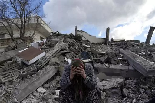 A woman sits on the rubble as emergency rescue teams search for people under the remains of destroyed buildings in Nurdagi town on the outskirts of Osmaniye city southern Turkey, Feb. 7, 2023. A year after the devastating 7.8 magnitude earthquake struck southern Turkey and northwestern Syria, a massive rebuilding effort is still trudging along. The quake caused widespread destruction and the loss of over 59,000 lives. (AP Photo/Khalil Hamra, File)