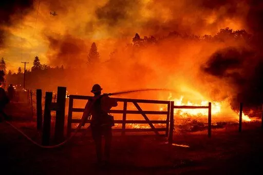 A firefighter extinguishes flames as the Oak Fire crosses Darrah Rd. in Mariposa County, Calif., on July 22, 2022. Crews were able to to stop it from reaching an adjacent home. (AP Photo/Noah Berger, File)