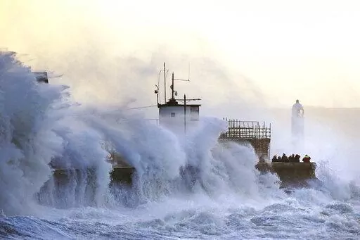 Waves crash against the sea wall and Porthcawl Lighthouse in Porthcawl, Bridgend, Wales, Britain, as Storm Eunice makes landfall Friday, Feb. 18, 2022. Millions of Britons are being urged to cancel travel plans and stay indoors Friday amid fears of high winds and flying debris as the second major storm this week prompted a rare “red” weather warning across southern England. ( Jacob King/PA via AP)