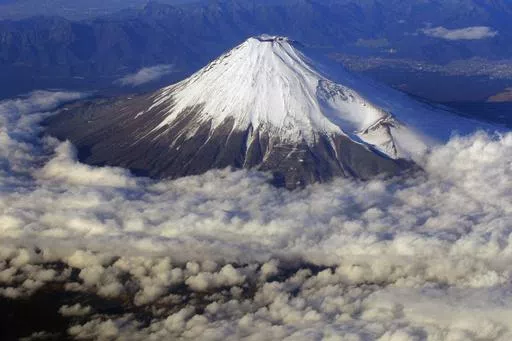 In this Dec. 8, 2010 file photo, snow-covered Mount Fuji, Japan's highest peak at 3,776-meters tall (12,385 feet), is seen from an airplane window. Those who want to climb one of the most popular trails of the iconic Japanese Mount Fuji will now have to reserve ahead and pay a fee as the picturesque stratovolcano struggles with overtourism, littering and those who attempt rushed “bullet climbing,” putting lives at risk. (AP Photo/Itsuo Inouye, File)