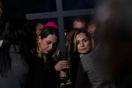 Two nurses, Albina from Russia, right, and Irina, from Ukraine hold the cross as they take part in the Via Crucis (Way of the Cross) torchlight procession presided by Pope Francis on Good Friday in front of Rome's Colosseum, in Rome, Friday, April 15, 2022. (AP Photo/Gregorio Borgia)