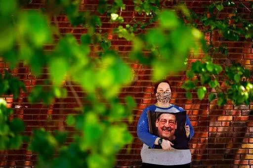 Sara Atkins poses for a photo, in Wynnewood, Pa., Tuesday, May 10, 2022, while holding a pillow with an image of her father Andy Rotman-Zaid, who died of COVID-19 in December 2020. She channels her grief into fighting for global vaccination and better access to health care to honor her father. (AP Photo/Matt Rourke)