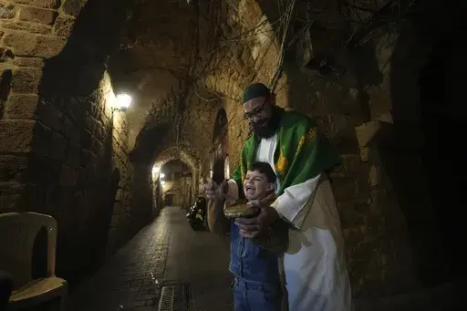 Mahmoud Fanas, a "musaharati,"or "dawn caller," who beats on a drum to wake up Muslims for a meal before sunrise during Ramadan, teaches a boy how to beat on drum as walks through old streets in the southern Lebanese port city of Sidon, Lebanon, Sunday, March 16, 2025. (AP Photo/Hassan Ammar)