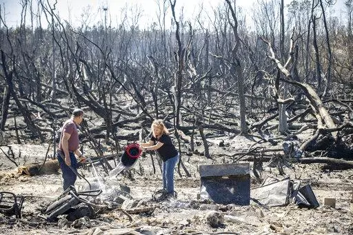 Hector Rivera and Wandi Blanco put water on hotspots behind their home in Panama City, Fla., Saturday, March 5, 2022, following a wildfire that started Friday. The fire destroyed two homes next to them and melted the siding off of their home. (Mike Fender/News Herald via AP)