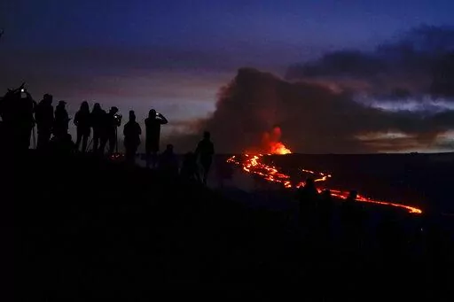 People watch and record images of lava from the Mauna Loa volcano Thursday, Dec. 1, 2022, near Hilo, Hawaii. (AP Photo/Gregory Bull)