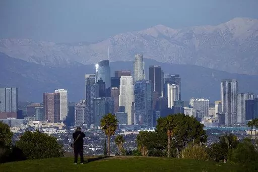 A visitor takes in a view of the city's skyline under the snow-covered San Gabriel mountains after a series of storms Thursday, March 2, 2023, in Los Angeles. (AP Photo/Marcio Jose Sanchez)