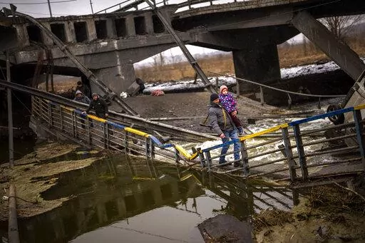 Local militiaman Valery, 37, carries a child as he helps a fleeing family across a bridge destroyed by artillery, on the outskirts of Kyiv, Ukraine, Wednesday, March 2. 2022.  Russian forces have escalated their attacks on crowded cities in what Ukraine's leader called a blatant campaign of terror. (AP Photo/Emilio Morenatti)