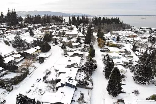 In this photo taken from a drone, snow covers streets, sidewalks and homes where nearly a foot of snow fell over the weekend, Monday, Dec. 27, 2021, in a neighborhood near Bellingham Bay in Bellingham, Wash. Emergency warming shelters were opened throughout western Washington and Oregon as temperatures plunged into the teens and forecasters said an arctic blast would last for several days. (AP Photo/Elaine Thompson)