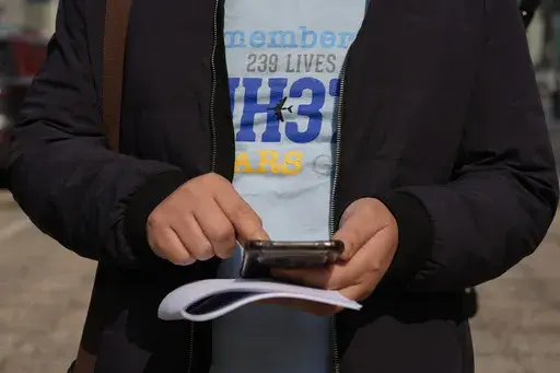 Jiang Hui, whose mother was on the missing MH370 Malaysia Airline passenger jet, wears a shirt "Remembering 239 Lives, MH370" checks his phone after talking to media on the 11th anniversary of the jet going missing Saturday, March 8, 2025, in Beijing, China. (AP Photo/Ng Han Guan)
