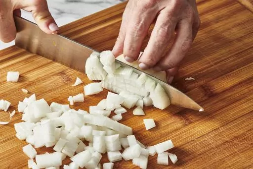 This Oct. 2022 image shows an onion being chopped in New York. There are lots of ways to reduce the amount of wasted food at home. Start by making a meal plan and purchasing just the foods you have plans for. Make a shopping list and avoid impulse buys that might languish in your fridge. (Cheyenne Cohen via AP)