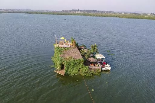 A floating restaurant and bar is seen from the air in Lake Victoria near the Luzira area of Kampala, Uganda Saturday, Feb. 18, 2023. Flowering plants rise from the water into the wooden hull of James Kateeba's boat, used as a floating restaurant and bar that can be unmoored to drift for pleasure, but the greenery emerges from an innovative recycling project which uses thousands of dirt-encrusted plastic bottles to anchor the boat. (AP Photo/Patrick Onen)