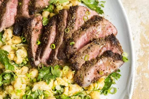 This image released by Milk Street shows a recipe for Spice-Crusted Steak with a side of partially mashed chickpeas. (Milk Street via AP)