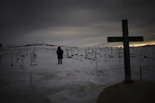 A woman walks at a graveyard covered by snow as the sun sets in Nuuk, Greenland, Sunday, Feb. 16, 2025. (AP Photo/Emilio Morenatti)