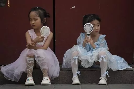 Children cool themselves with electric fans as they take a rest near the Forbidden City on a hot day in Beijing, June 25, 2023. The National Oceanic and Atmospheric Administration said Thursday, July 13, an already warming Earth steamed to its hottest June on record. (AP Photo/Andy Wong, File)
