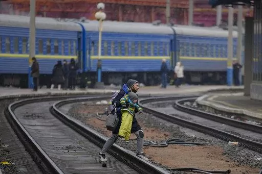 A woman carries a baby over the tracks trying to board a Lviv bound train, in Kyiv, Ukraine, Thursday, March 3, 2022. Ukrainian President Volodymyr Zelenskyy's office says a second round of talks with Russia aimed at stopping the fighting that has sent more than 1 million people fleeing over Ukraine's borders, has begun in neighboring Belarus, but the two sides appeared to have little common ground. (AP Photo/Vadim Ghirda)