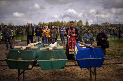 A priest blesses the remains of three people who died during the Russian occupation and were disinterred from temporary burial sites in Bucha, on the outskirts of Kyiv, on Wednesday, April 27, 2022. (AP Photo/Emilio Morenatti)