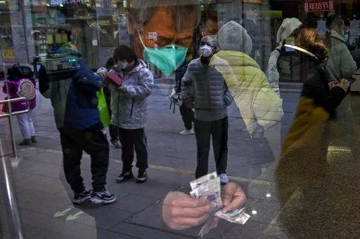 Visitors are reflected on a window pane as a man counts Chinese currency notes at a shop selling tea in Qianmen, a popular tourist spot in Beijing, Tuesday, Jan. 3, 2023. As the virus continues to rip through China, global organizations and governments have called on the country start sharing data while others have criticized its current numbers as meaningless. (AP Photo/Andy Wong)