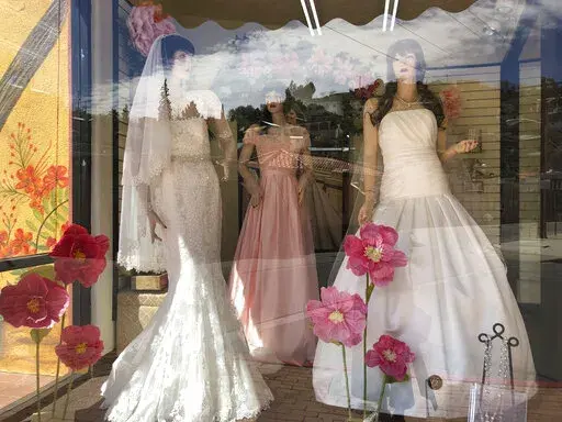 Mannequins in wedding gowns are seen in a window display on March 15, 2021, at a bridal store in Nogales, Ariz.  The holidays are a popular time to get engaged, and that means many couples are diving into 2022 by touring wedding venues, researching vendors and carefully crafting guest lists. Planning a wedding can be a time that’s filled with emotions, expectations and the pressure to create a perfect event — all of that combined makes it far too easy to overspend.  (AP Photo/Suman Naishadha