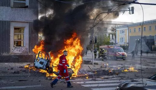 A medical worker runs past a burning car after a Russian attack in Kyiv, Ukraine, Monday, Oct. 10, 2022. The Russian missiles that rained down Monday on cities across Ukraine, bringing fear and destruction to areas that had seen months of relative calm, are an escalation in Moscow's war against its neighbor. But military analysts say it’s far from clear whether the strikes mark a turning point in a war that has killed thousands of Ukrainians and sent millions fleeing from their homes. (AP Phot