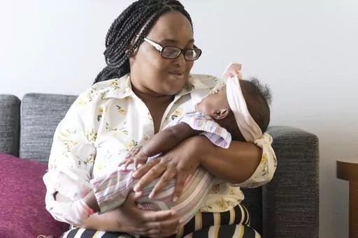 Asian Davis, 33, of Sikeston, Mo., cradles her 8-month-old daughter, Mira White during an interview on Oct. 3, 2023, in St. Louis. Davis and her lawyers say Mira suffered brain damage in March after developing bacterial meningitis tied to powdered infant formula contaminated with Cronobacter sakazakii, a germ known to cause severe disease in young babies. (AP Photo/Michael Thomas)