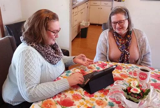 Helen Rottier, 25, shows her mother, Amy Rottier, 50, how she organizes her calendar on her iPad while sitting at the dining room table of her family’s home in Madison, Wis., on Wednesday, Jan. 26, 2022. The two women illustrate the way Gen Xers and millennials differ in how they spent their time on an average day as young adults because of changes in technology and patterns in forming families over the last two decades. (AP Photo/Scott Bauer).
