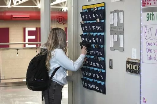 A ninth grader places her cellphone in to a phone holder as she enters class at Delta High School, Friday, Feb. 23, 2024, in Delta, Utah. Most schools have policies regulating student cellphone use at school. But the reality is kids don’t always follow the rules and schools enforce them sporadically. (AP Photo/Rick Bowmer, File)